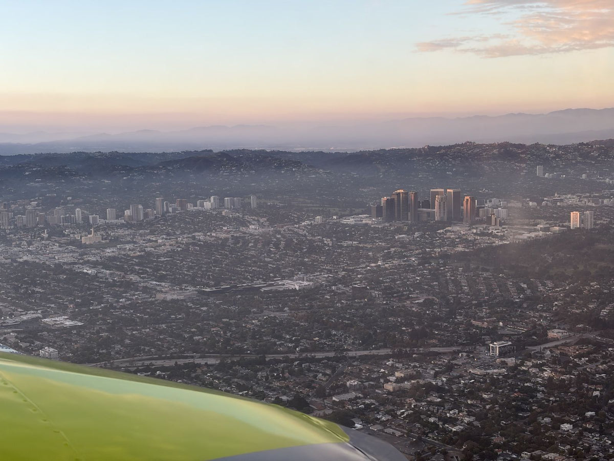 Century City towers and the Westside of Los Angeles at sunset, seen over the wing of a small airplane with the hills and mountains behind