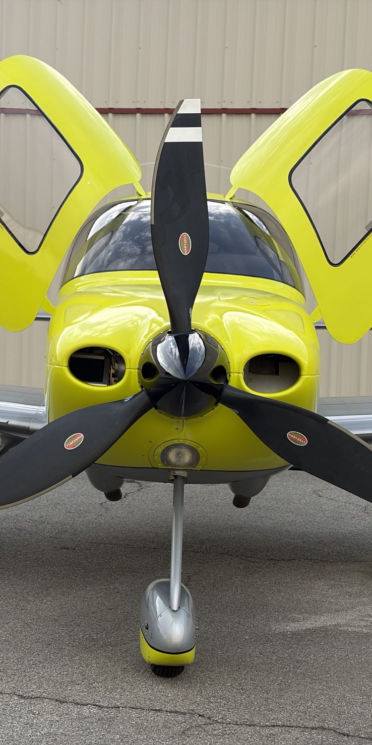 Cirrus aircraft head-on with both doors raised in front of a hangar
