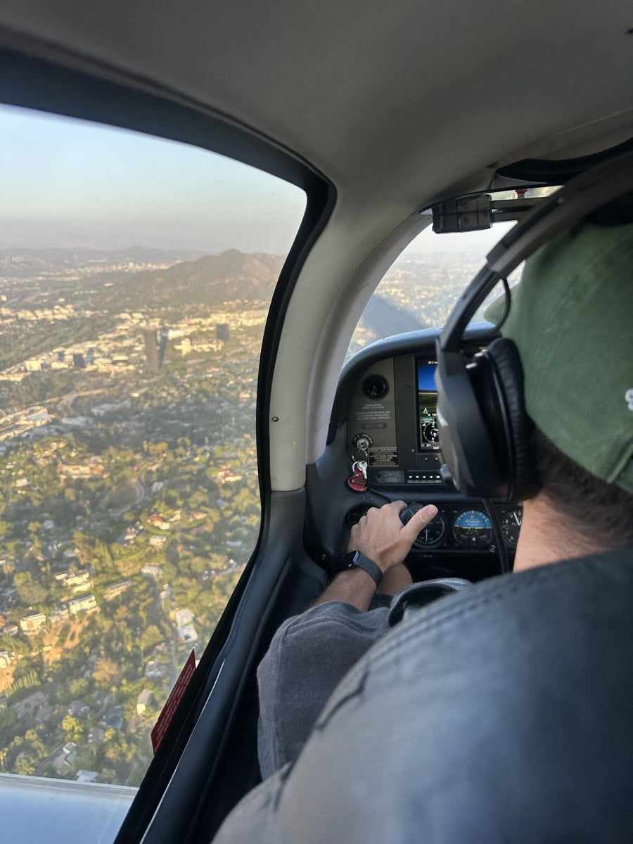 A discovery flight guest in a headset flying a Cirrus over the Hollywood Hills with a hand on the controls, seen from the back seat