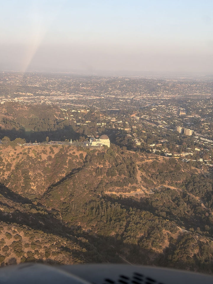 Griffith Observatory and its white domes on the ridge of Mount Hollywood in Griffith Park, seen from a small airplane, with the Los Angeles basin stretching to the horizon