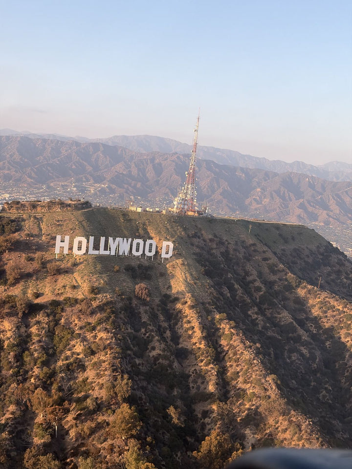 The Hollywood Sign on the slope of Mount Lee, seen almost level with the letters from a small airplane, with the radio tower on the summit and the San Gabriel Mountains in the distance