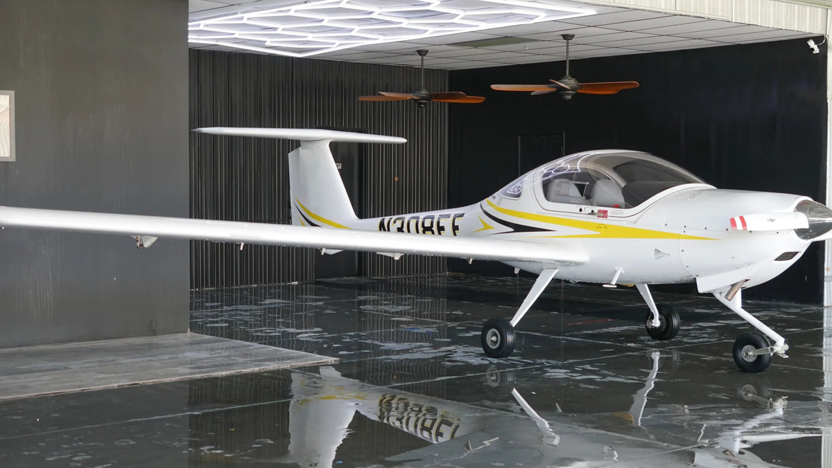 Diamond DA20-C1 in side profile on a glossy hangar floor, with its long low wing and T-tail